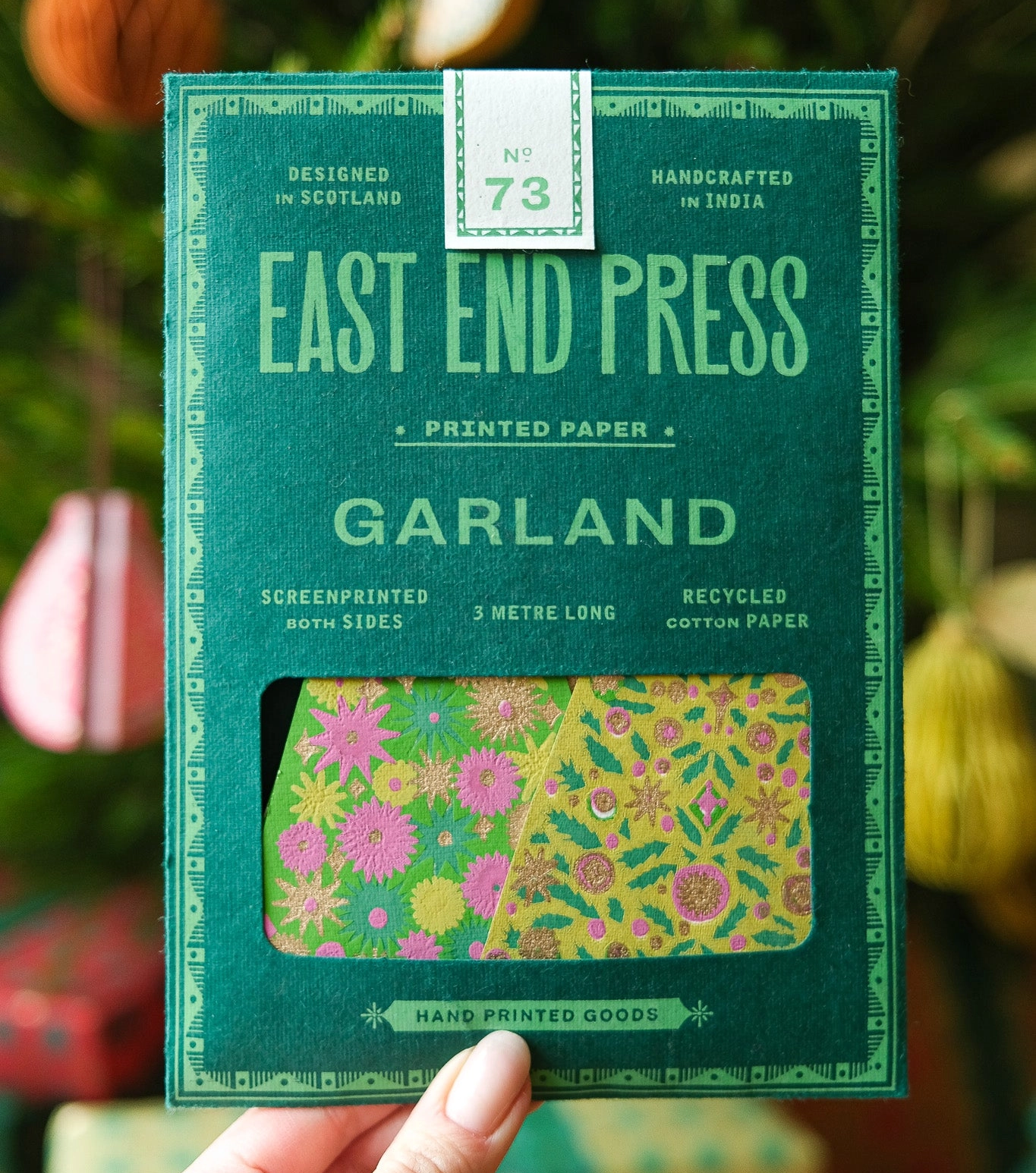Handheld package of East End Press Garland printed paper with decorative elements in the background.