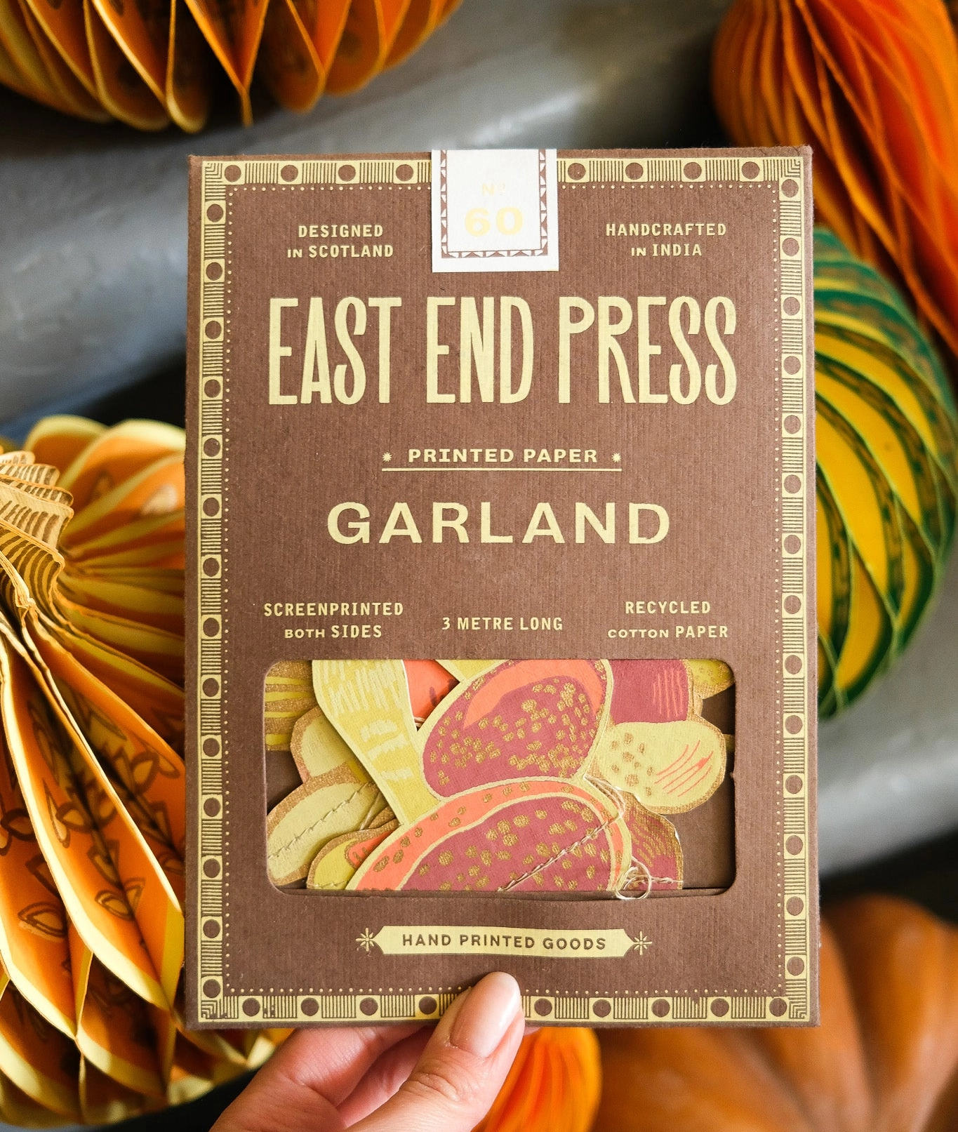Hand holding a package of 'East End Press Garland' printed paper mushrooms with paper pumpkins in the background.